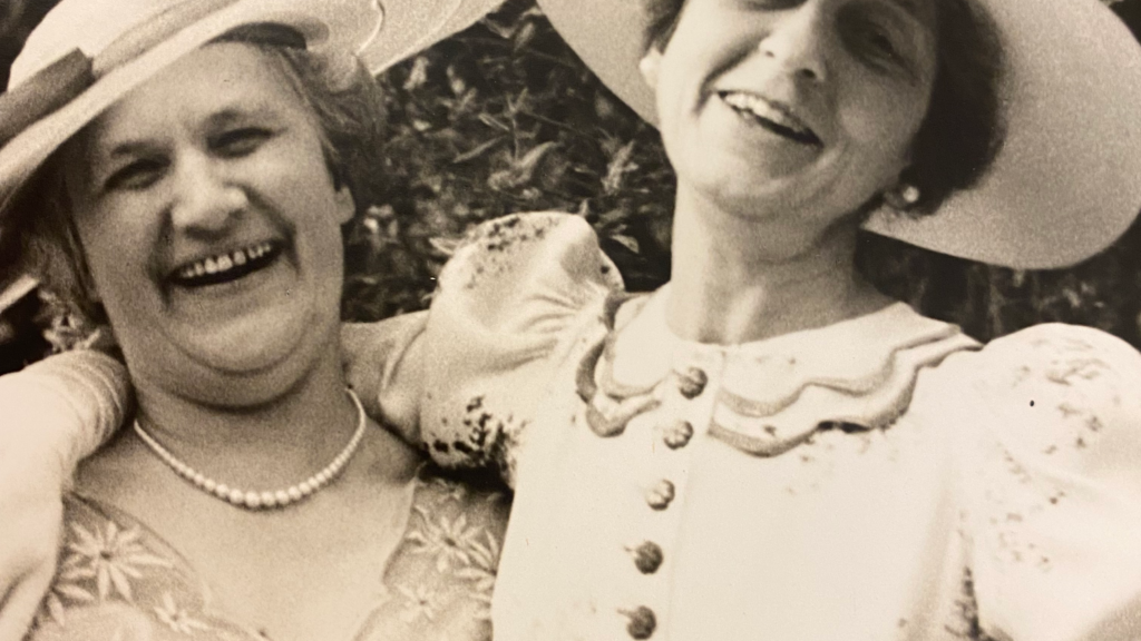Historical 1937 black and white photograph of Stella Elkins Tyler wearing a wide-brimmed hat and vintage dress smiling with a companion outdoors
