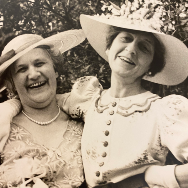 Historical 1937 black and white photograph of Stella Elkins Tyler wearing a wide-brimmed hat and vintage dress smiling with a companion outdoors